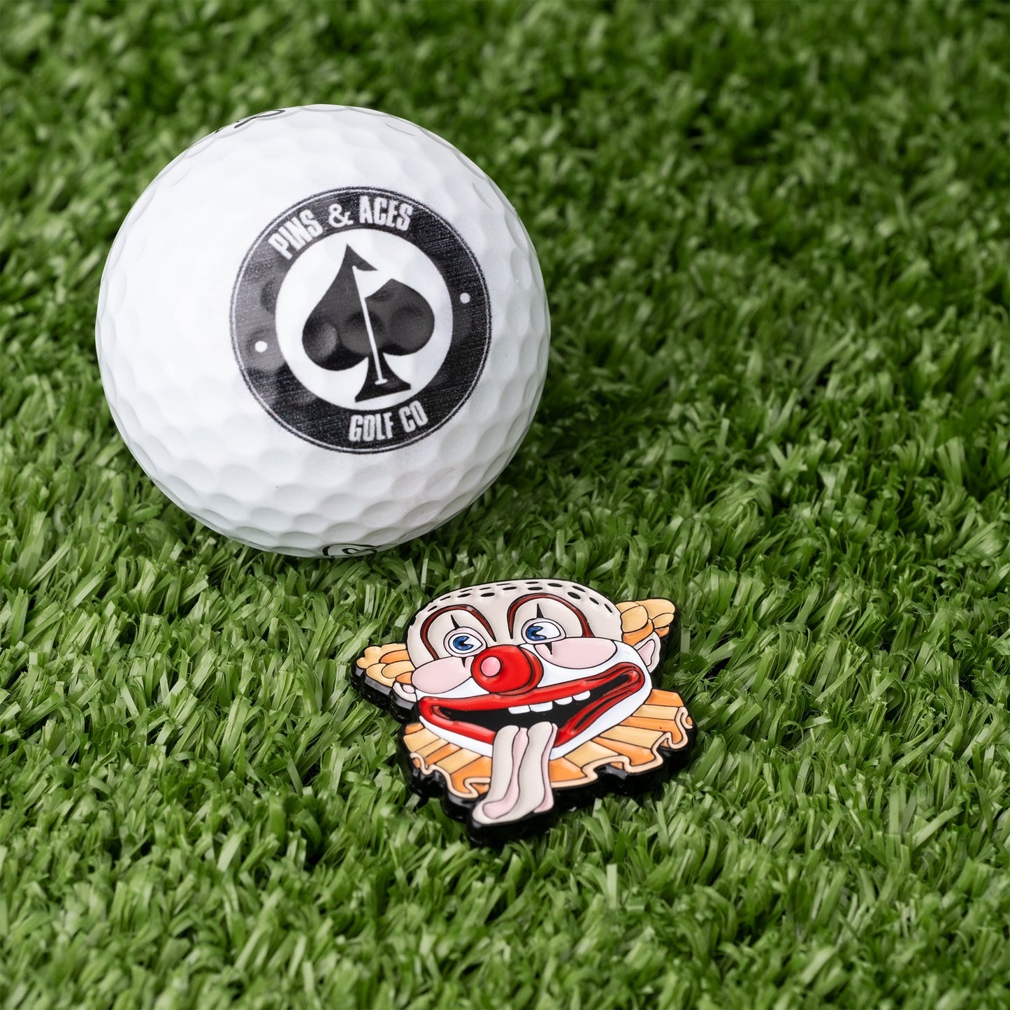 Colorful Clown Mouth ball marker next to a golf ball on a green surface.