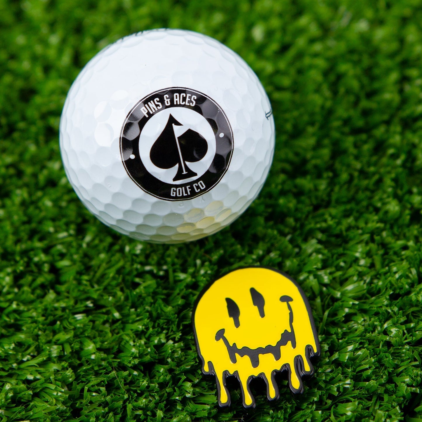 Melting face ball marker with a colorful, smiling design on a green background.
