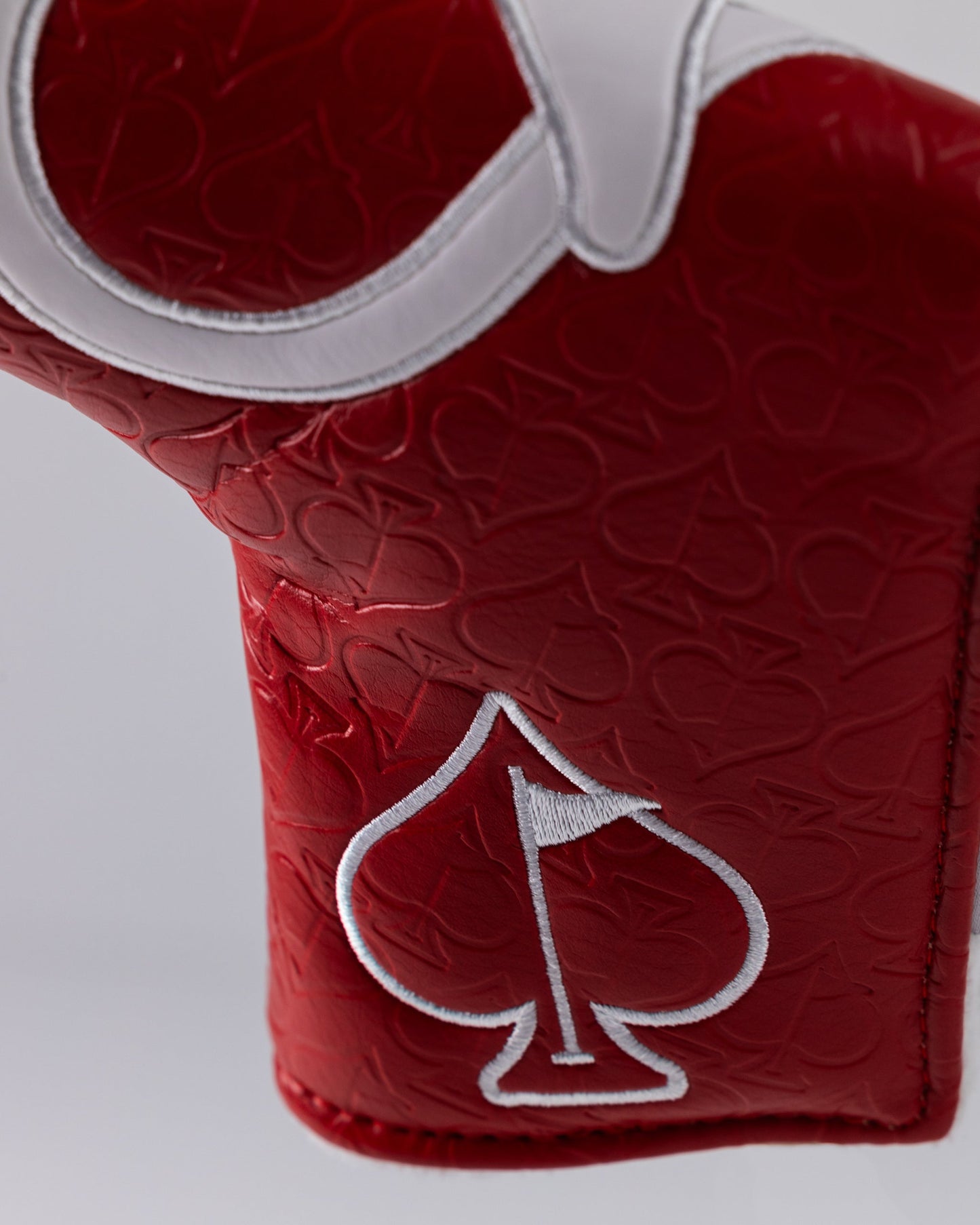 Close-up of a bold red golf club headcover with embossed spade pattern and white embroidered spade logo.