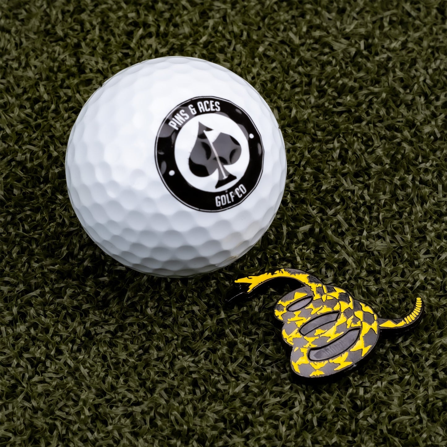 Bold golf ball marker featuring a yellow snake design, placed next to a textured golf ball on a green turf background.
