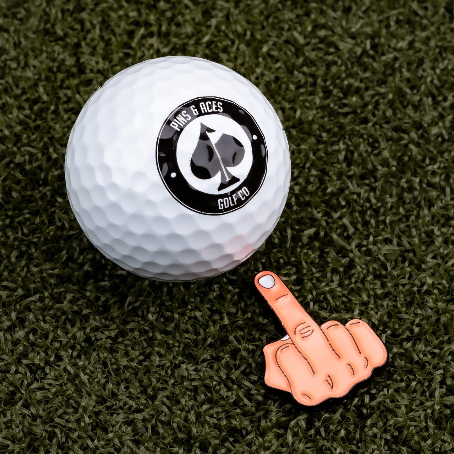 Bold middle finger ball marker next to a golf ball, perfect for golfers who want to express their personality on the course.