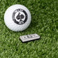 Cash Stack Ball Marker next to a golf ball on green turf, featuring a unique design for stylish golfing.