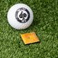 Cheese cracker ball marker next to a golf ball on green turf, showcasing a fun and unique golf accessory.