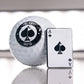Close-up of an Ace of Spades golf ball marker next to a golf ball with the logo "Pins & Aces Golf Co" on a reflective surface.