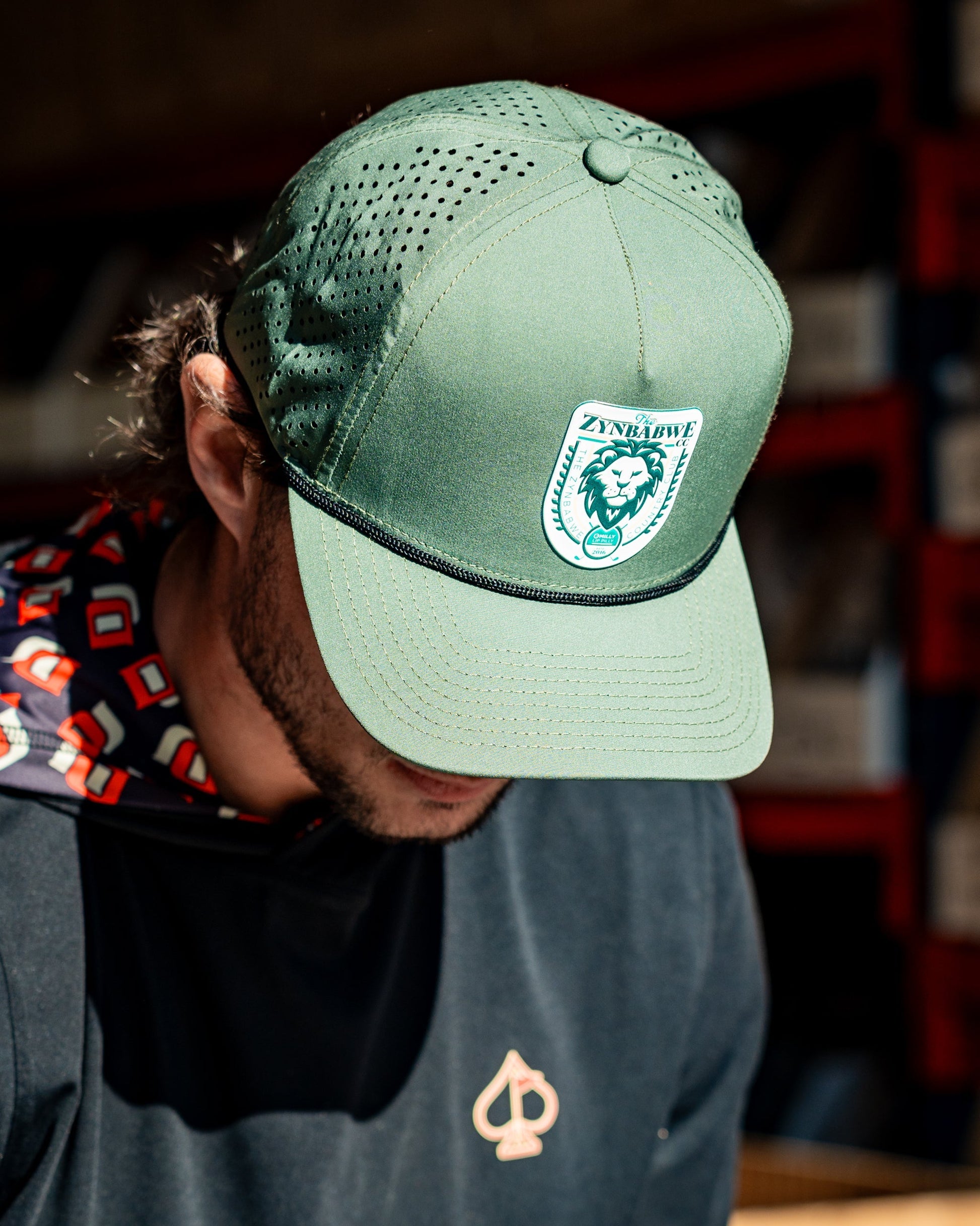 Perforated olive rope hat featuring Zynbabwe Country Club branding.