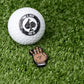 Chubs Hand Ball Marker next to a golf ball on a grass surface, showcasing its design and size.