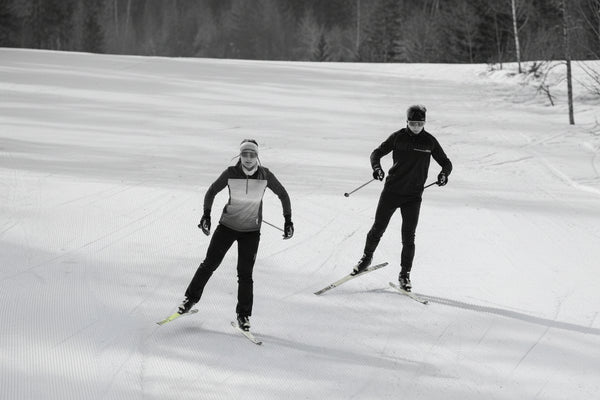 Two skiers on a snowy slope with trees in the background