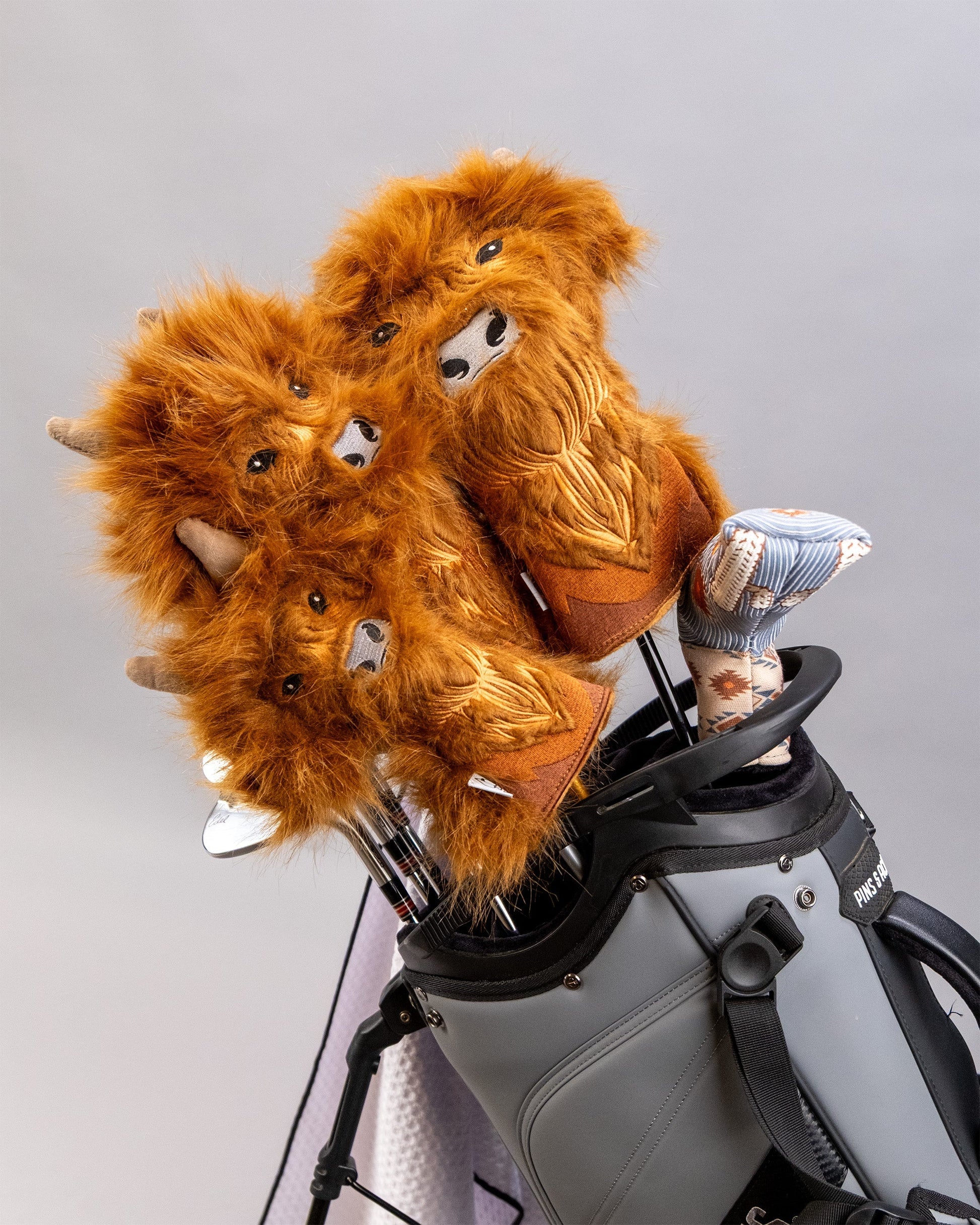 Highland Cow driver cover set with plush, furry cow faces and patterned socks, placed in a golf bag for protection.