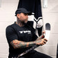 Man sitting in a locker room holding a hockey stick, wearing a black TPS shirt.