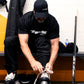 Person tying their shoes in a locker room with hockey equipment.