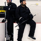 Two men in hockey gear sitting on a bench with hockey sticks.