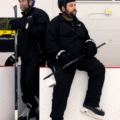 Two men in hockey gear sitting on a bench with hockey sticks.