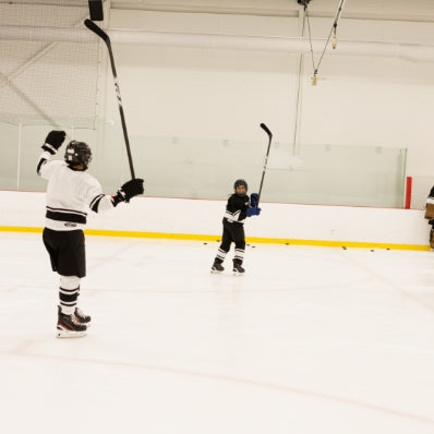 Two hockey players on an ice rink with one player holding a stick above their head.