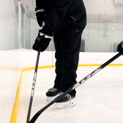 Person on an ice rink holding a hockey stick, wearing black hockey gear.
