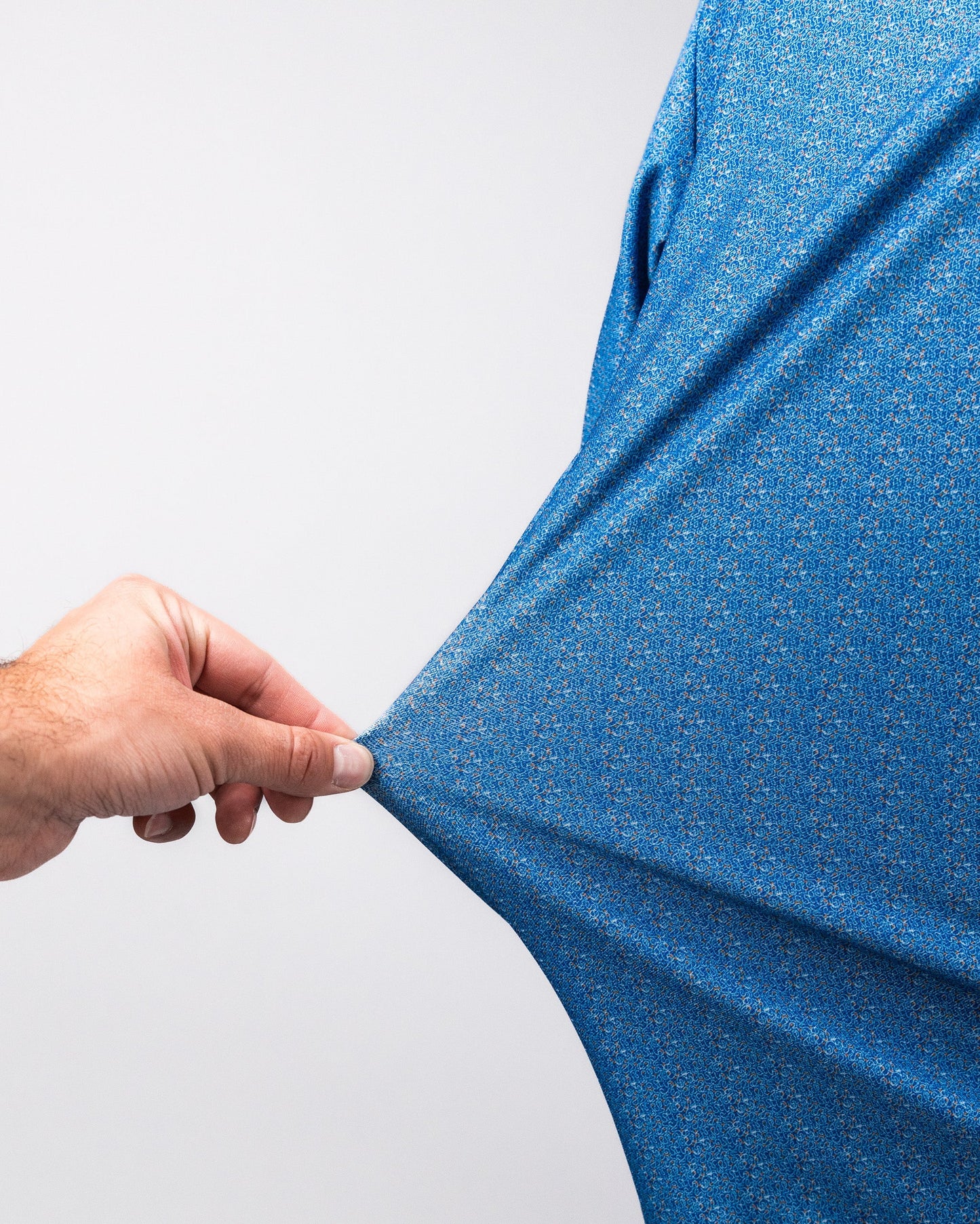 Close-up of a hand stretching a blue Player Preferred™ Polo - Cosmic Swirl fabric, showcasing its vibrant, textured pattern.