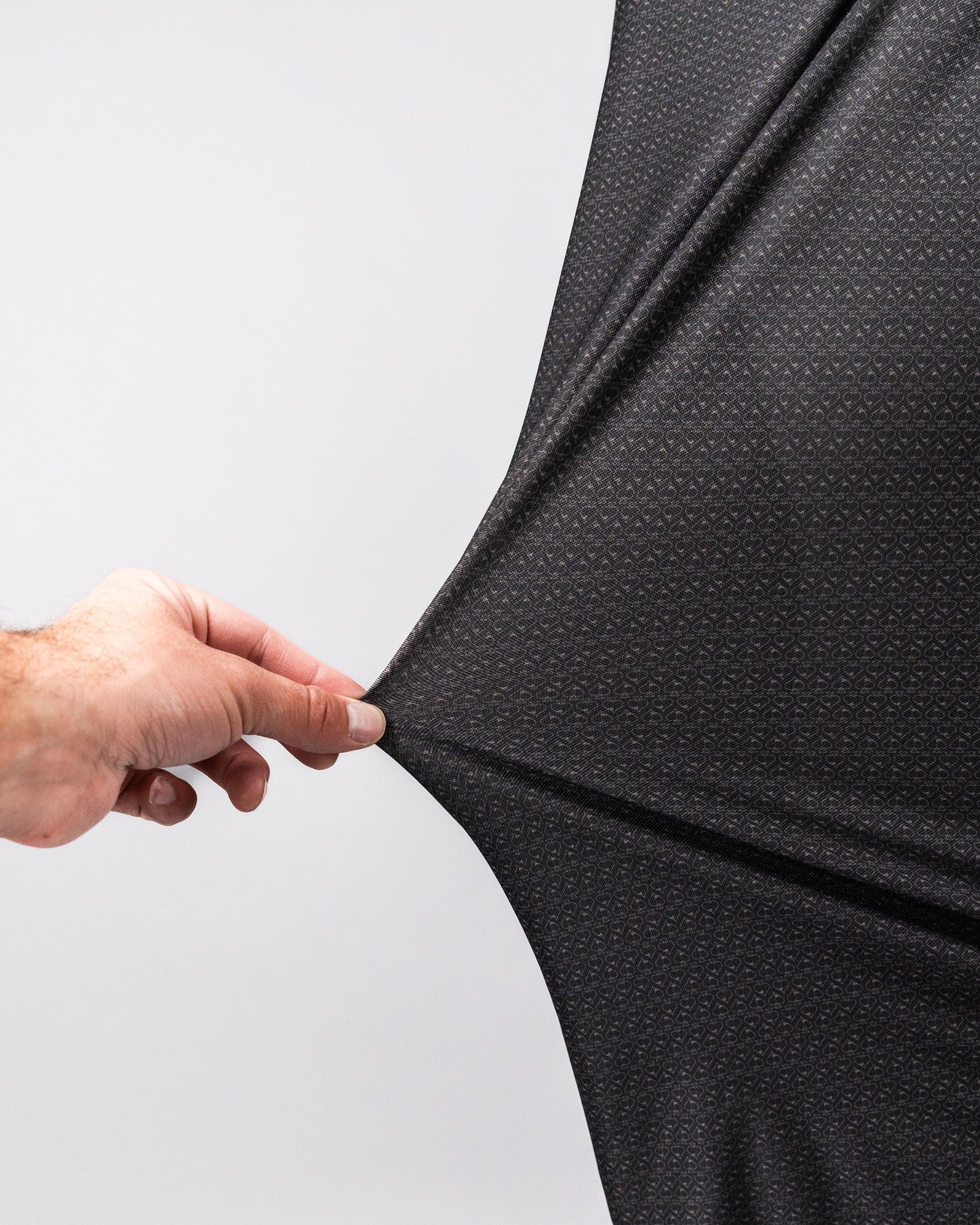 Close-up of a hand stretching a black Player Preferred™ Polo Midnight Spade fabric, showing its stretch and texture.