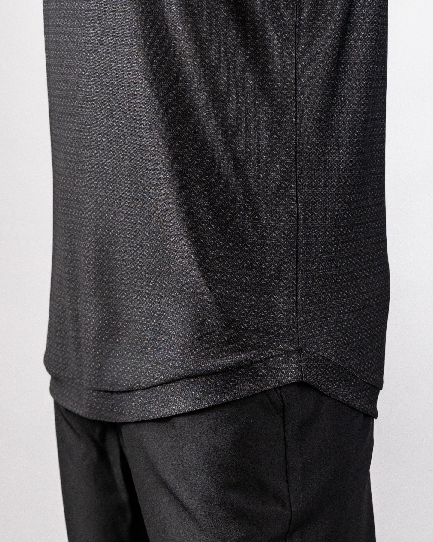 Close-up of a black polo shirt with a subtle, intricate pattern, paired with black pants, showcasing a stylish, modern look.