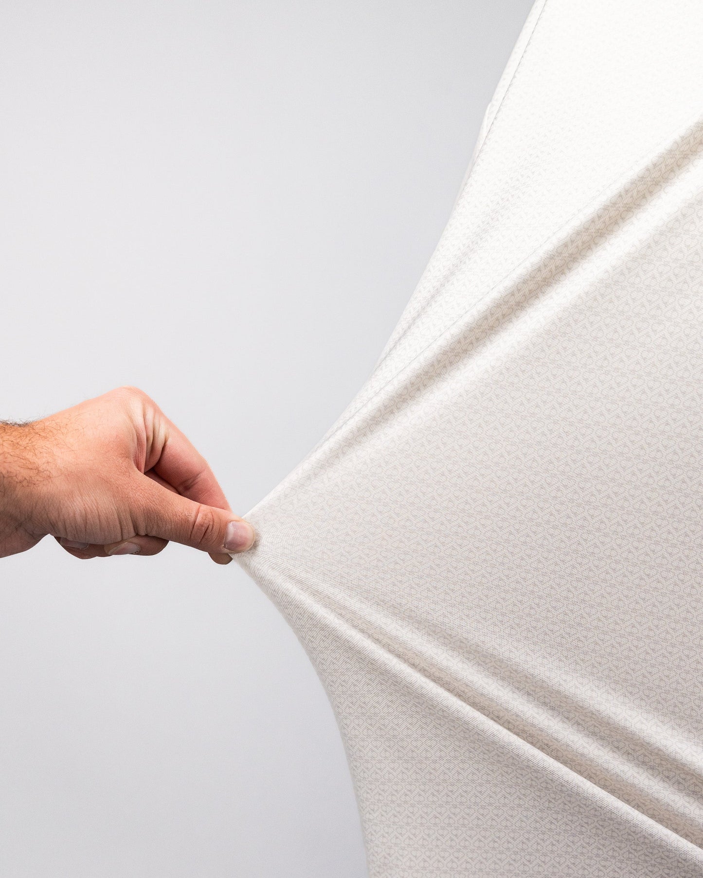 Close-up of a hand stretching a white Player Preferred™ Polo - Vapor Spade fabric, showing its stretchability and texture.