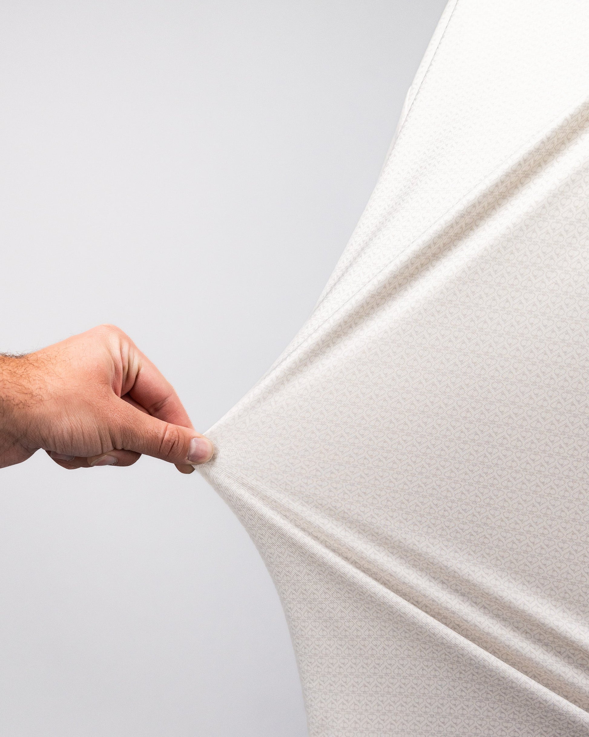 Close-up of a hand stretching a white Player Preferred™ Polo - Vapor Spade fabric, showing its stretchability and texture.