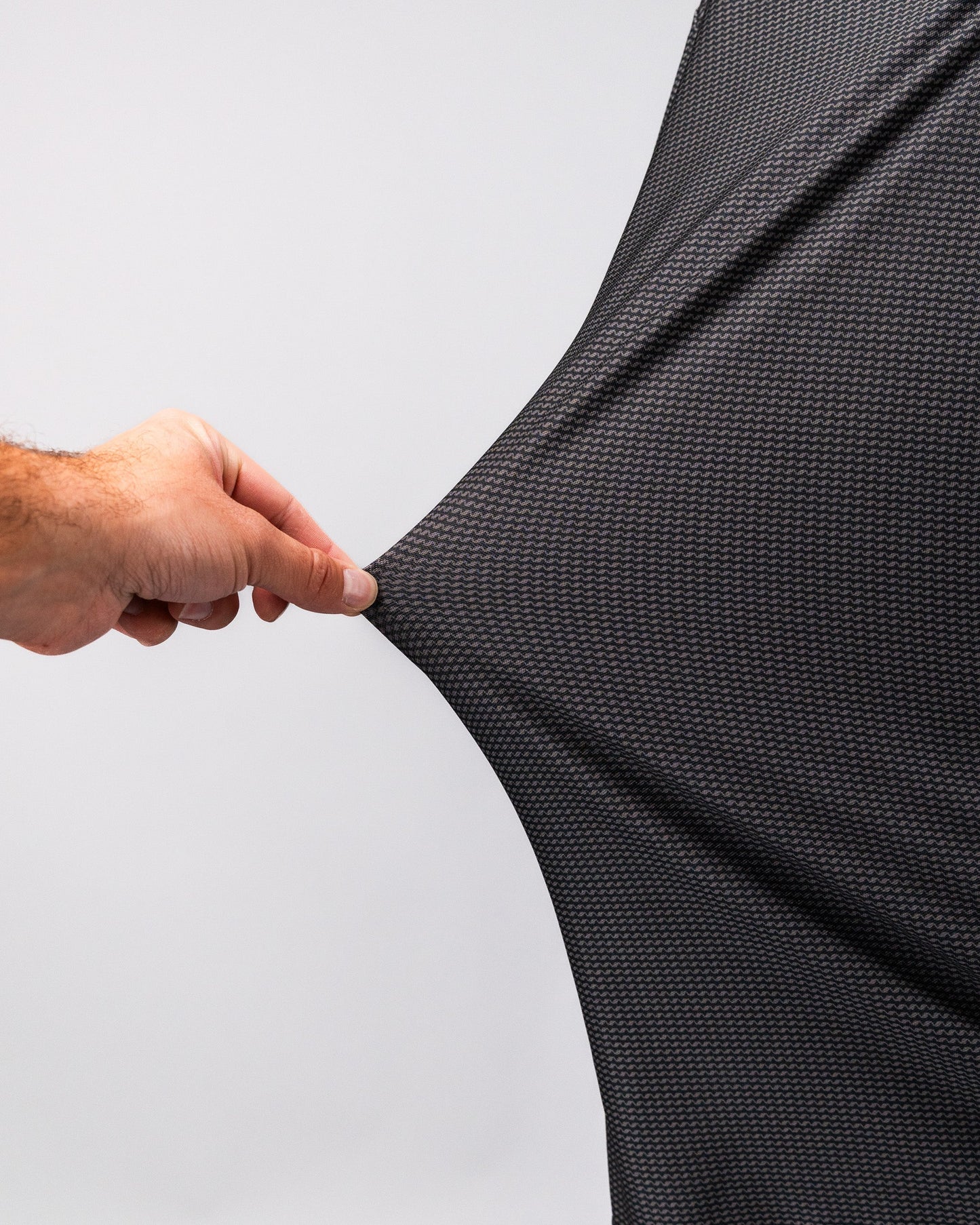 Close-up of a hand stretching the black and gray patterned Player Preferred™ Polo - Night Wave fabric.