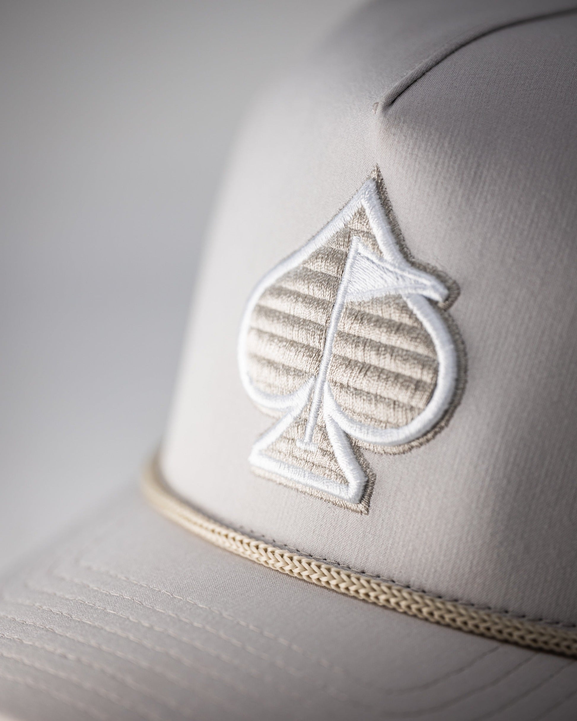 Perforated rope hat in bone color featuring a textured spade logo and a stylish rope detail along the brim.