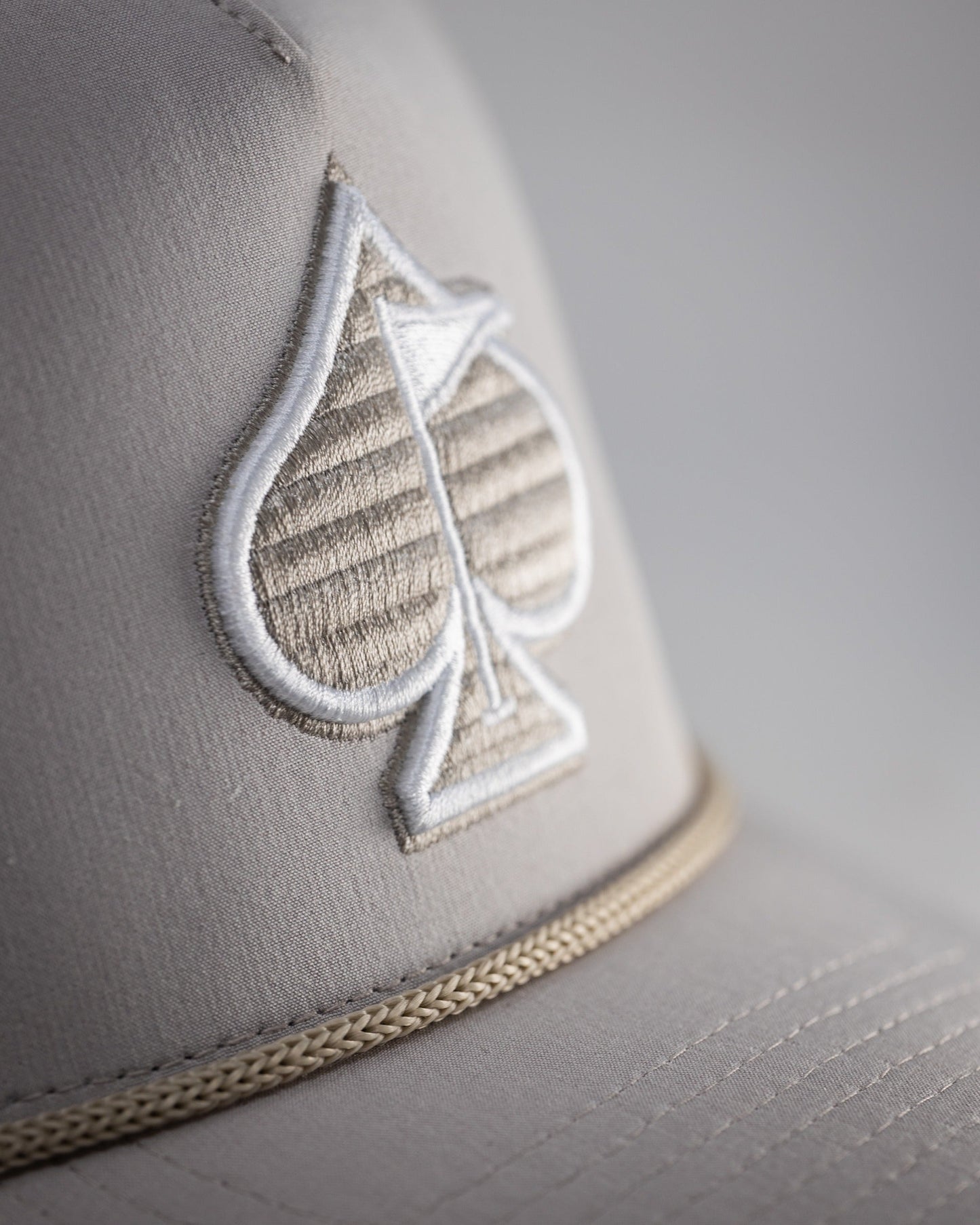 Perforated rope hat in bone color featuring a stylish embroidered spade logo and a classic rope detail.