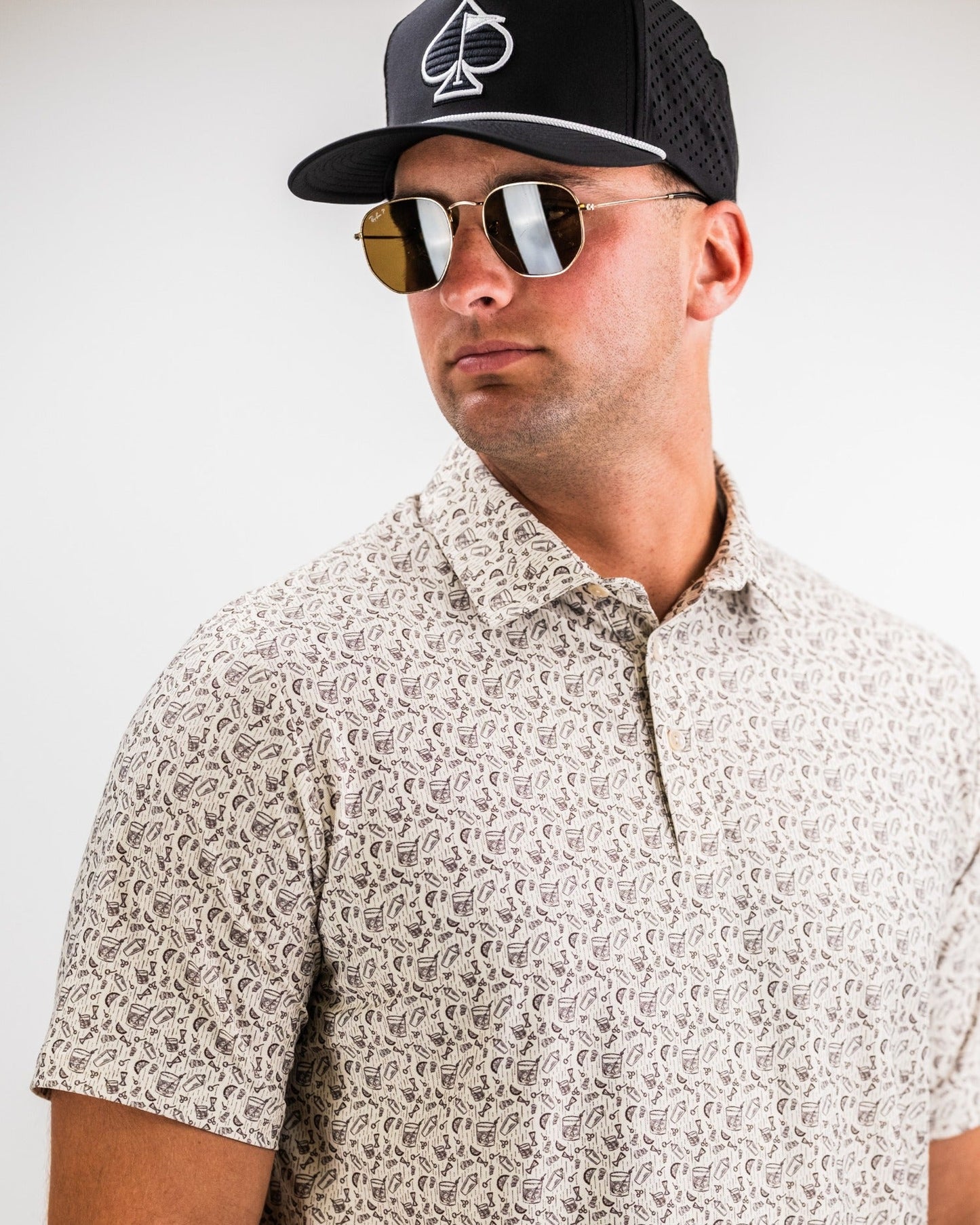 Stylish man wearing the Player Preferred™ Polo in Old Fashioned print, paired with sunglasses and a cap, showcasing bold golf fashion.
