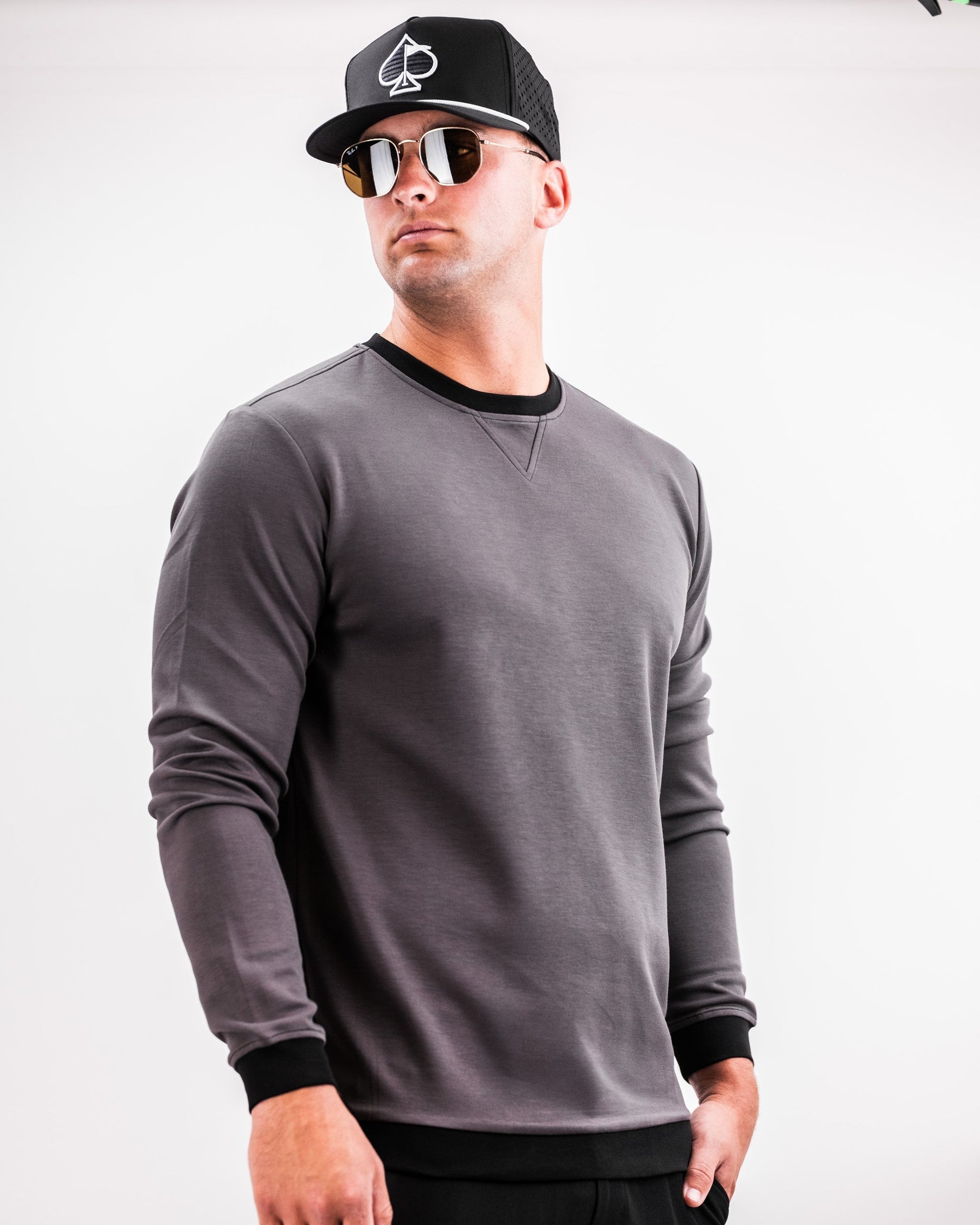 Male model wearing a slate grey Player Preferred™ Crewneck sweatshirt with black accents, black cap, and sunglasses, standing against a white background.