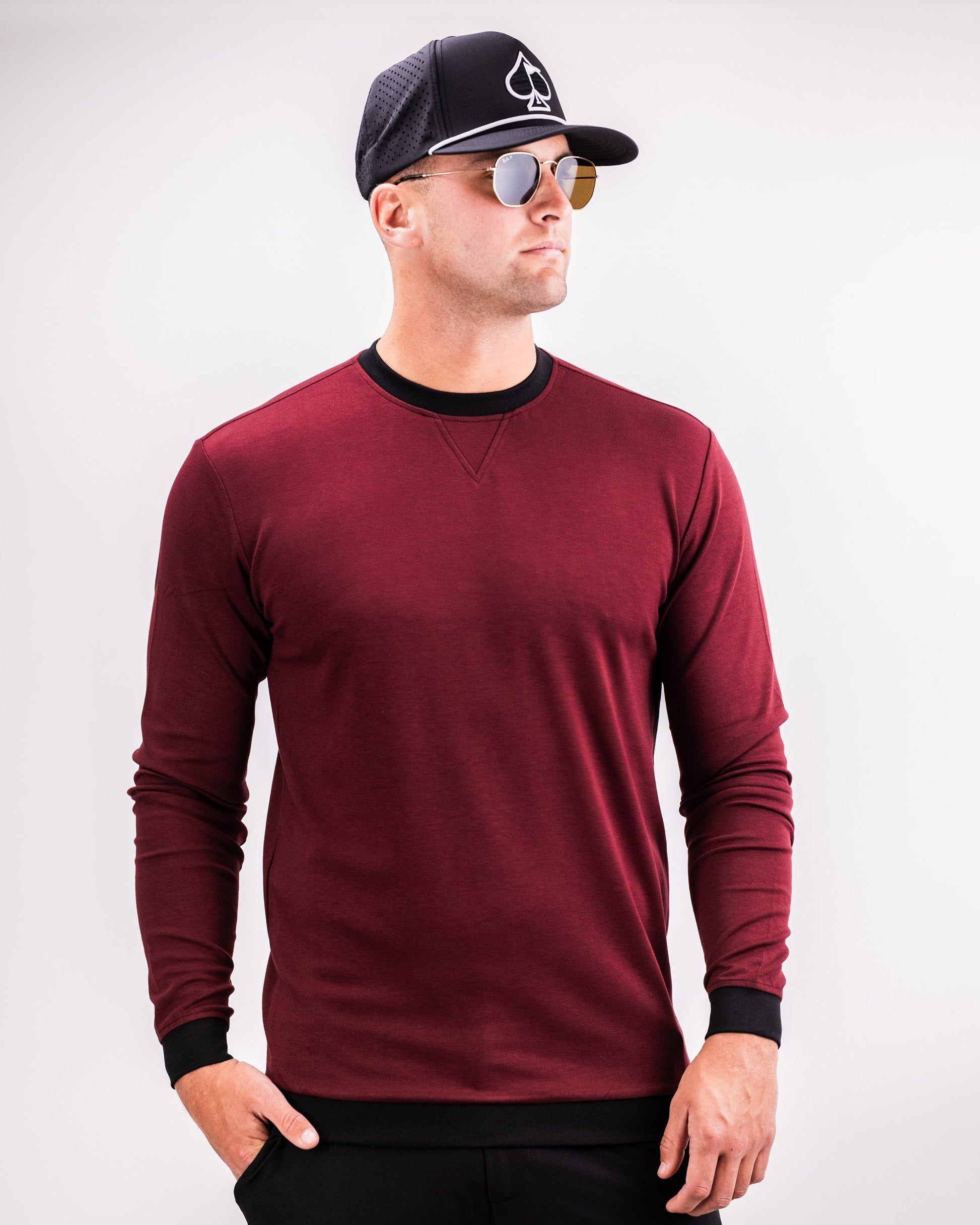 Male model wearing a maroon Player Preferred™ Crewneck in Merlot, paired with sunglasses, a black cap, and black pants.