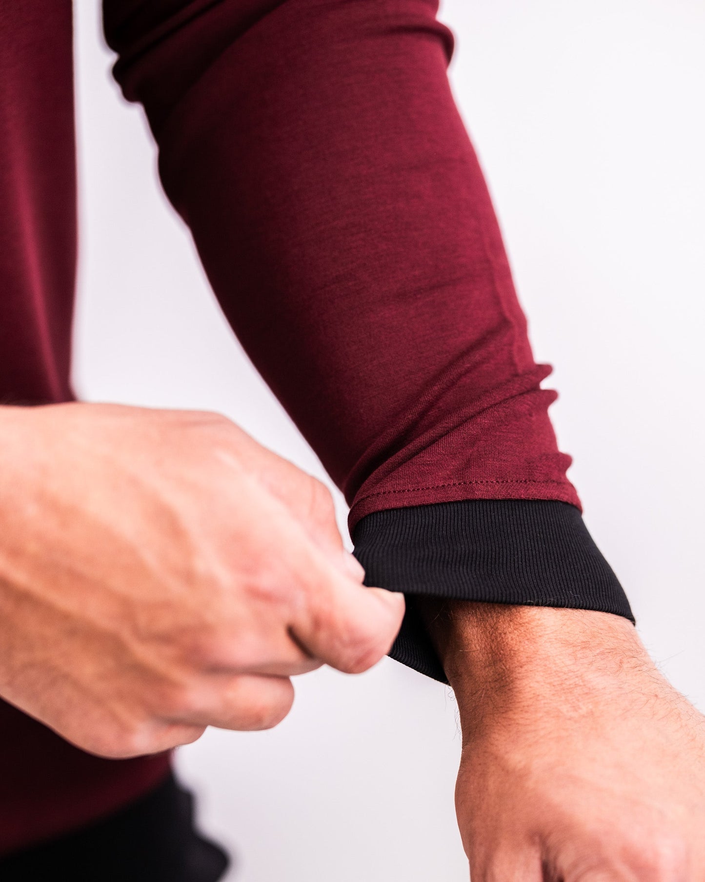 Close-up of a person adjusting the cuff of a maroon Player Preferred™ Crewneck with black trim, highlighting the fabric and fit.