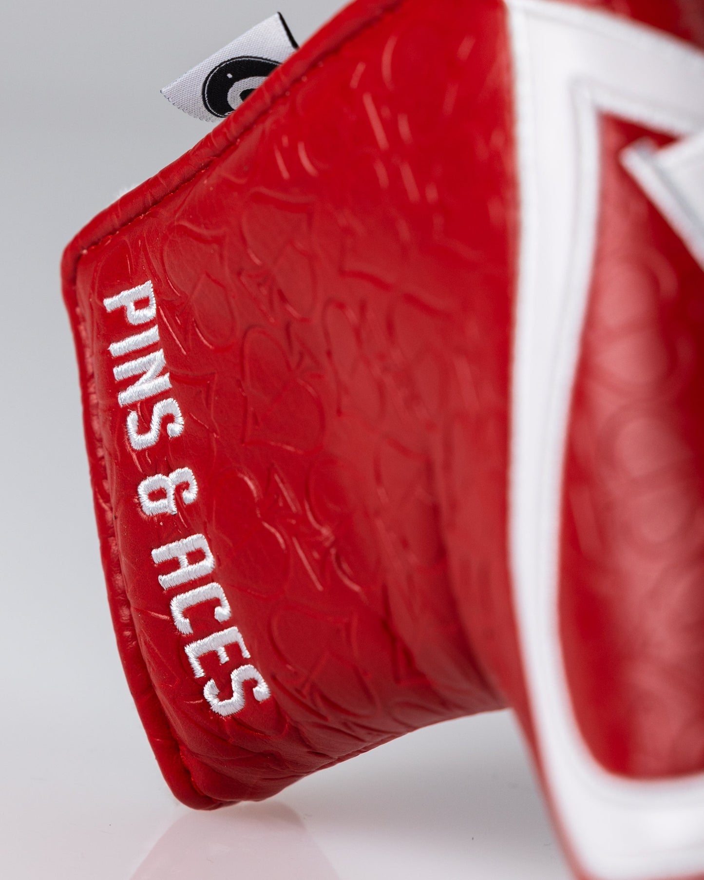 Red golf headcover with embossed pattern, white "PINS & PICS" embroidery, and a black and white logo tab.