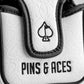Close-up of a white golf accessory with black trim, featuring a spade logo and "PINS & ACES" embroidery, bold and standout...