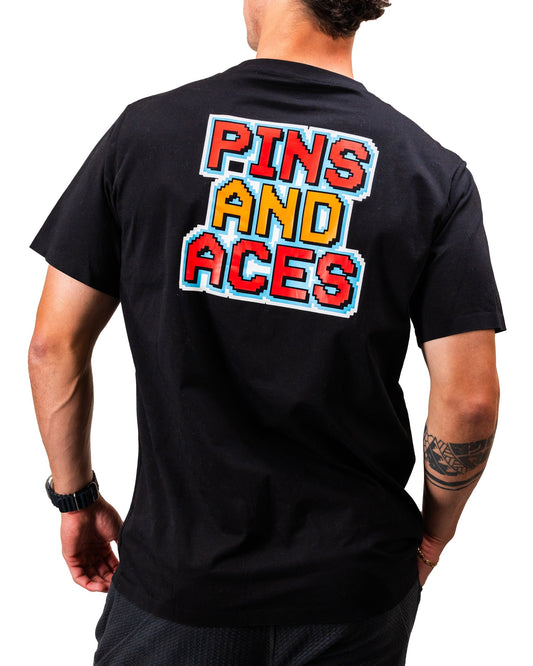 Man wearing a black t-shirt with vibrant 8-bit style graphic text "PINS AND ACES" on the back.