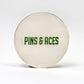 Alt text: "6 Milly - Wintergreen Ball Marker featuring a large, white, circular design with 'PINS & ACES' printed in green font centered on the surface."
