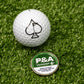 Alt text: "Close-up of a 6 Milly - Wintergreen Ball Marker, featuring a white golf ball with a black spade symbol on artificial grass next to a green and silver Wintergreen 6 marker disc with warning text."