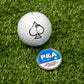 "6 Milly Cool Mint ball marker next to a golf ball with an ace of spades logo on a green turf background.