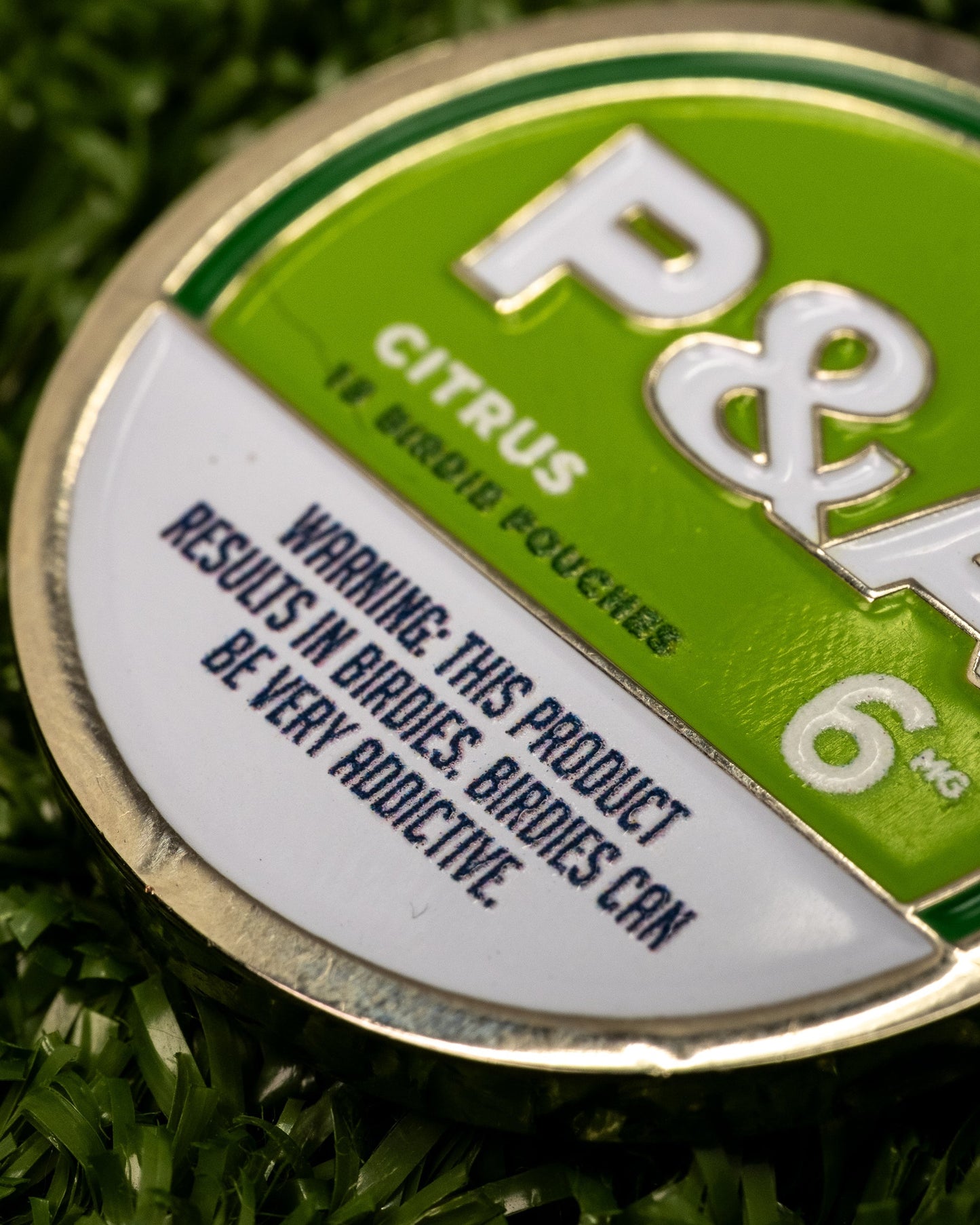 Close-up of a 6 Milly Citrus Ball Marker, featuring a warning about its addictive nature for birdie enthusiasts.