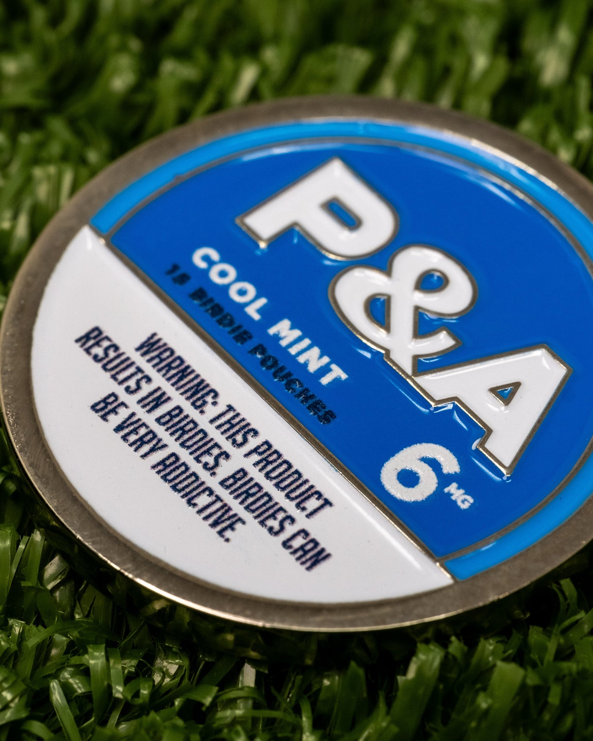 Close-up of a 6 Milly Cool Mint ball marker featuring a blue and silver design with warning label.